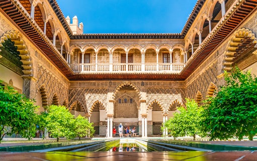 Tour group exploring Alcazar of Seville's Moorish architecture courtyard.