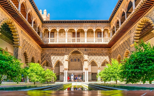 Tour group exploring Alcazar of Seville's Moorish architecture courtyard.