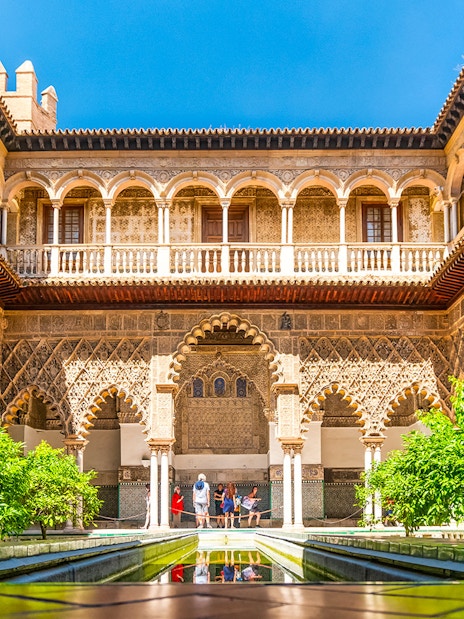 Tour group exploring Alcazar of Seville's Moorish architecture courtyard.