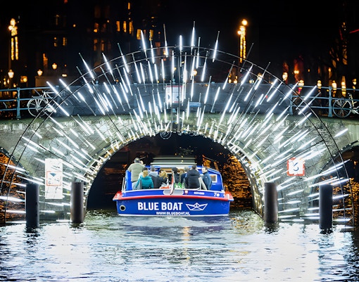 Canal boat passing under illuminated bridge during Amsterdam Light Festival.