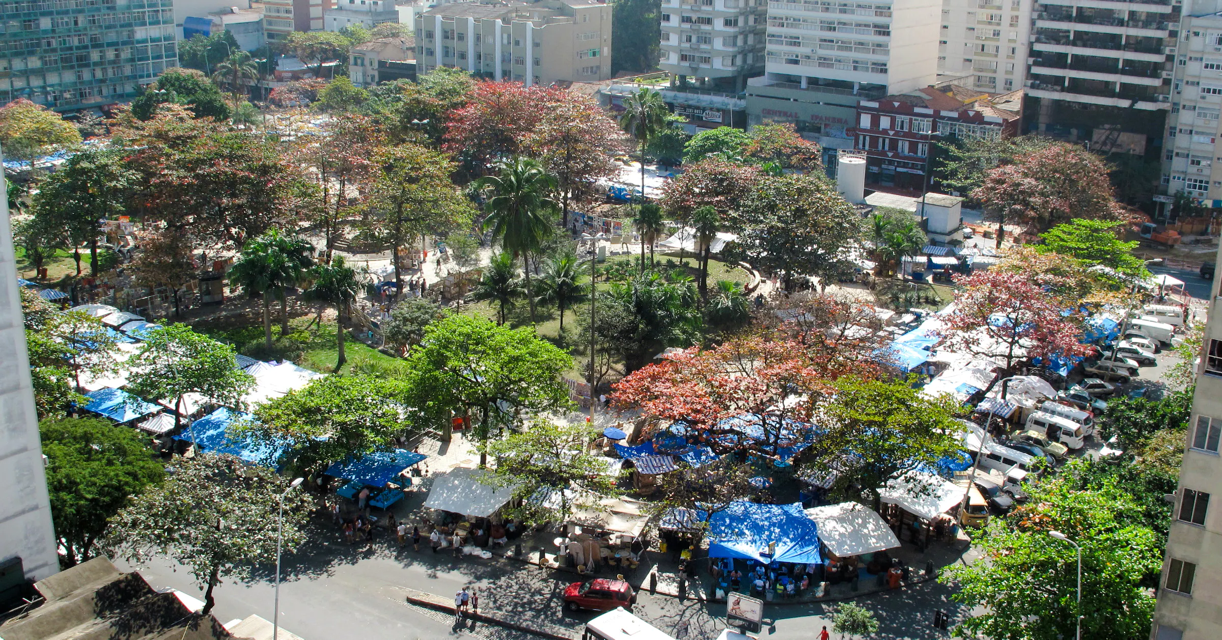 Outdoor market stalls at Ipanema Hippie Fair, Rio de Janeiro, surrounded by trees and city buildings.