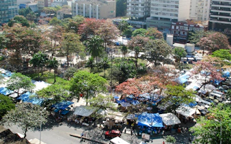 Outdoor market stalls at Ipanema Hippie Fair, Rio de Janeiro, surrounded by trees and city buildings.