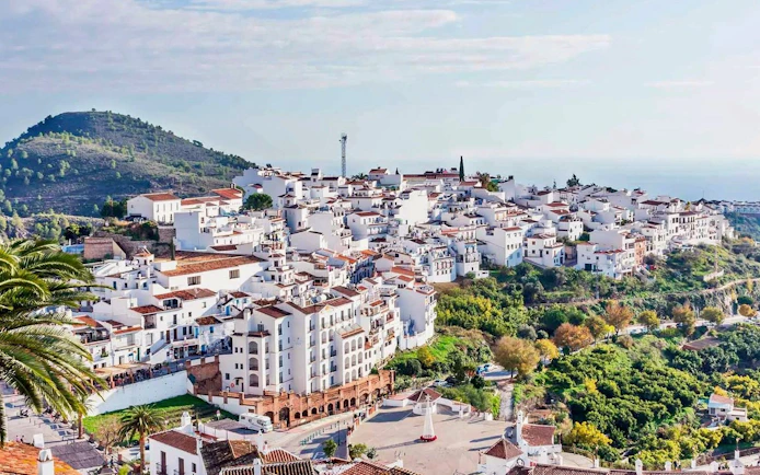 Whitewashed buildings in Frigiliana, Spain, nestled on a hillside with lush greenery.