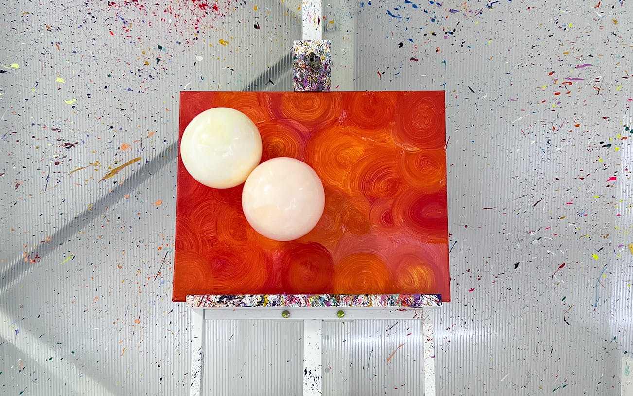 Balloon splatter art on canvas with vibrant orange swirls at workshop.