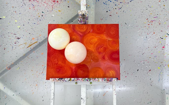 Balloon splatter art on canvas with vibrant orange swirls at workshop.