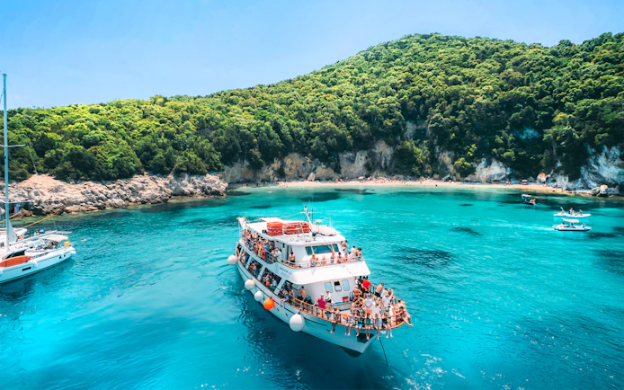 Cruise boat in Blue Lagoon with tourists enjoying the view near lush green hills, Lefkimmi.