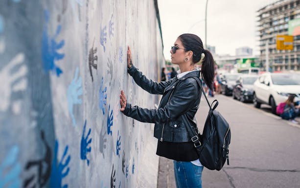 Woman viewing handprint graffiti on Berlin Wall.
