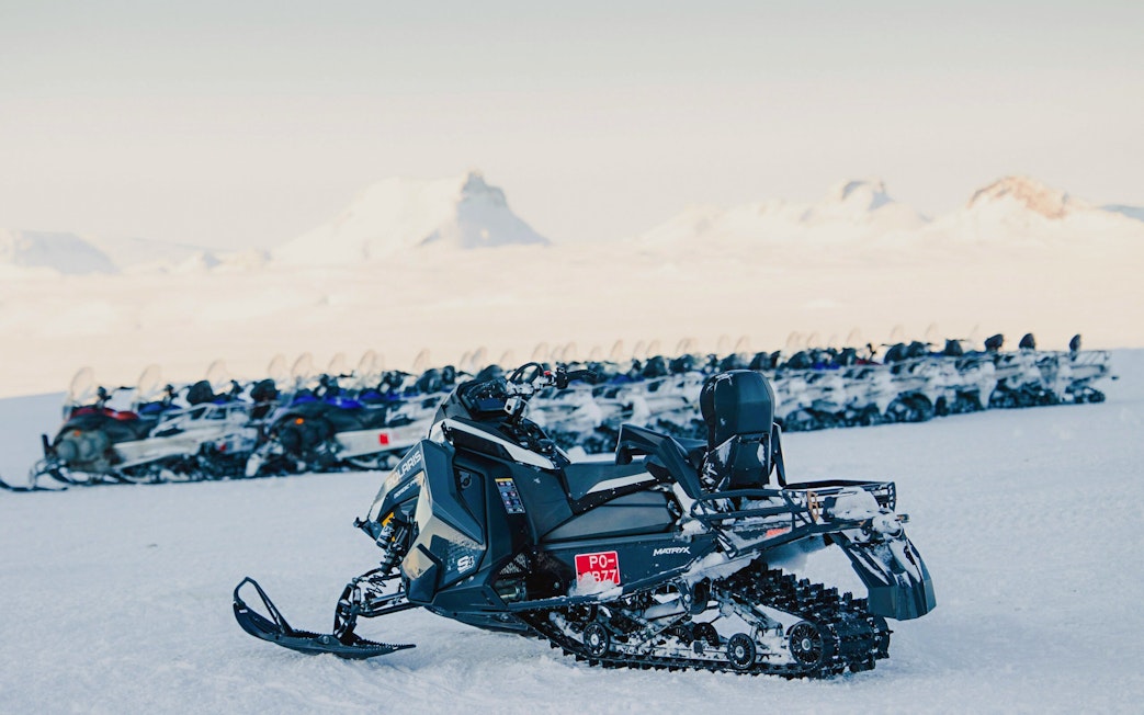 Snowmobiles lined up on snowy terrain near Gullfoss waterfall in Iceland.