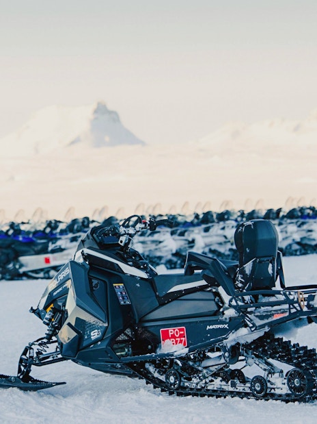 Snowmobiles lined up on snowy terrain near Gullfoss waterfall in Iceland.
