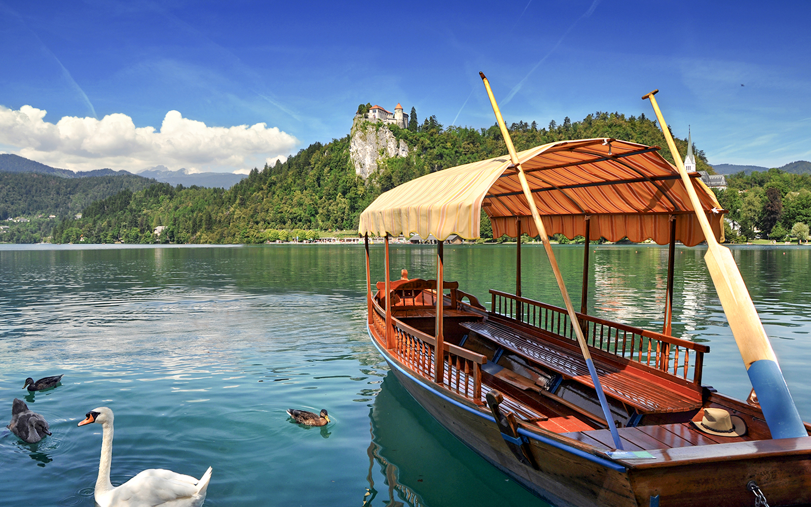 Bled Castle overlooking Lake Bled with a traditional wooden boat in the foreground.