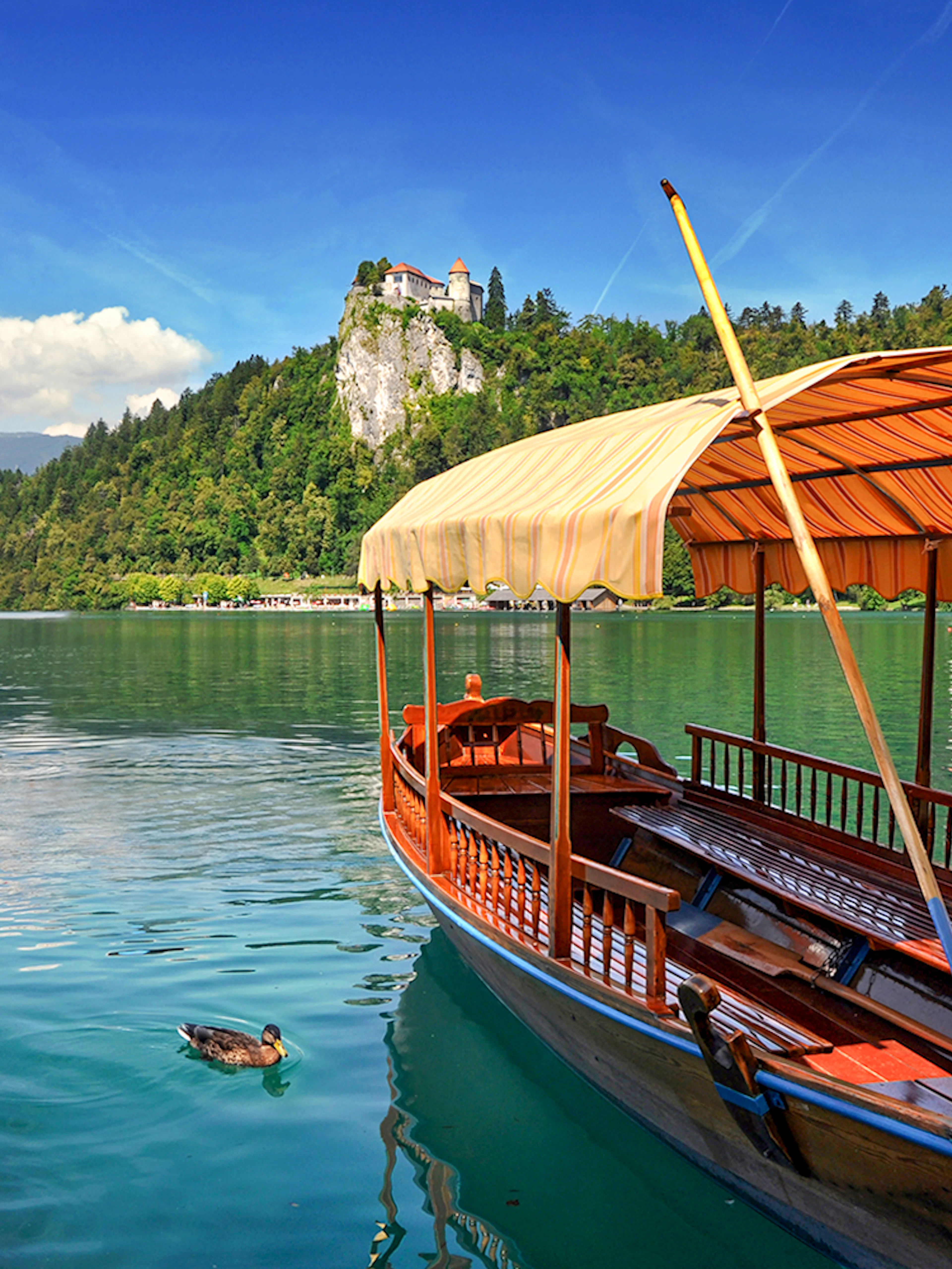 Bled Castle overlooking Lake Bled with a traditional wooden boat in the foreground.