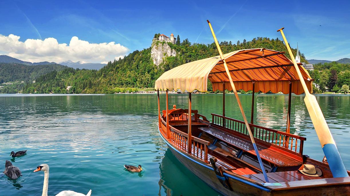 Bled Castle overlooking Lake Bled with a traditional wooden boat in the foreground.