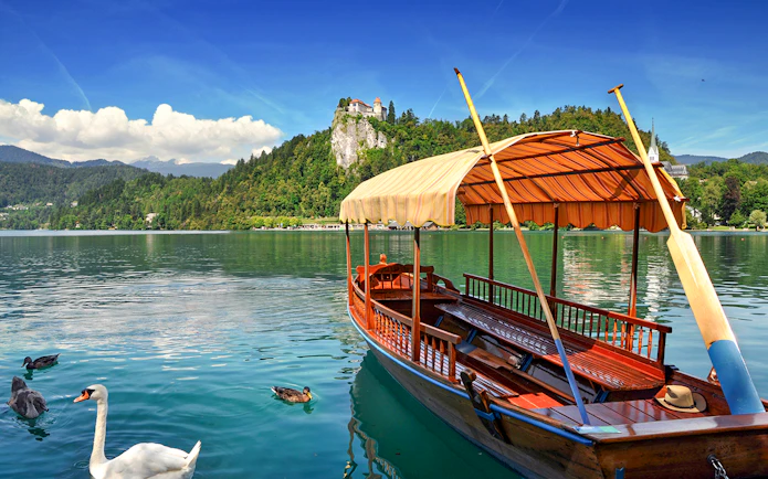 Bled Castle overlooking Lake Bled with a traditional wooden boat in the foreground.