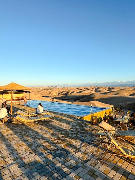 Desert camp with pool and seating area in Agafay, Marrakesh, overlooking dunes.