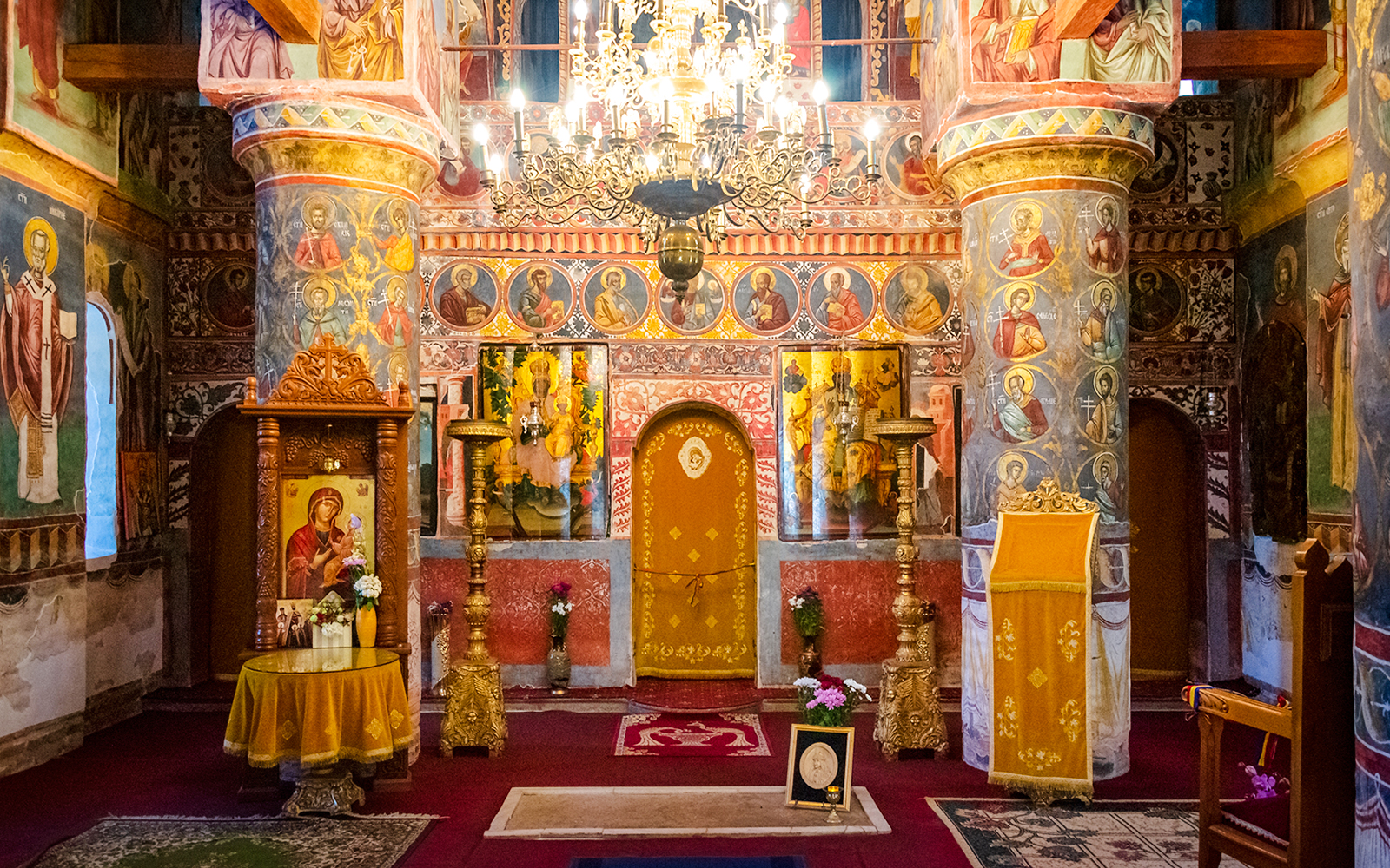 Interior of Snagov Monastery in Romania with ornate frescoes and golden chandeliers.