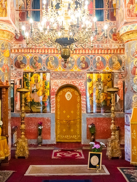 Interior of Snagov Monastery in Romania with ornate frescoes and golden chandeliers.
