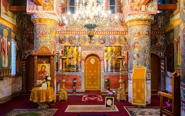 Interior of Snagov Monastery in Romania with ornate frescoes and golden chandeliers.