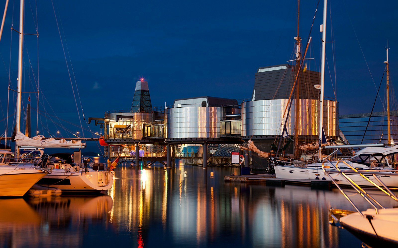 Norwegian Petroleum Museum at night with boats docked nearby.