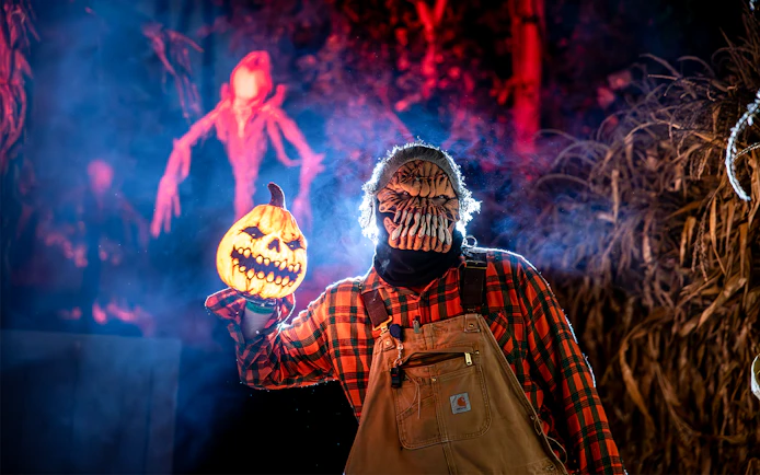 Performer in a mask holding a pumpkin lantern at Six Flags SCarowinds Snicker's Halloween Event.