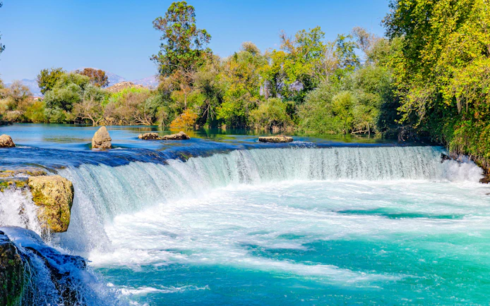 Manavgat Waterfalls cascading over rocks surrounded by lush greenery.