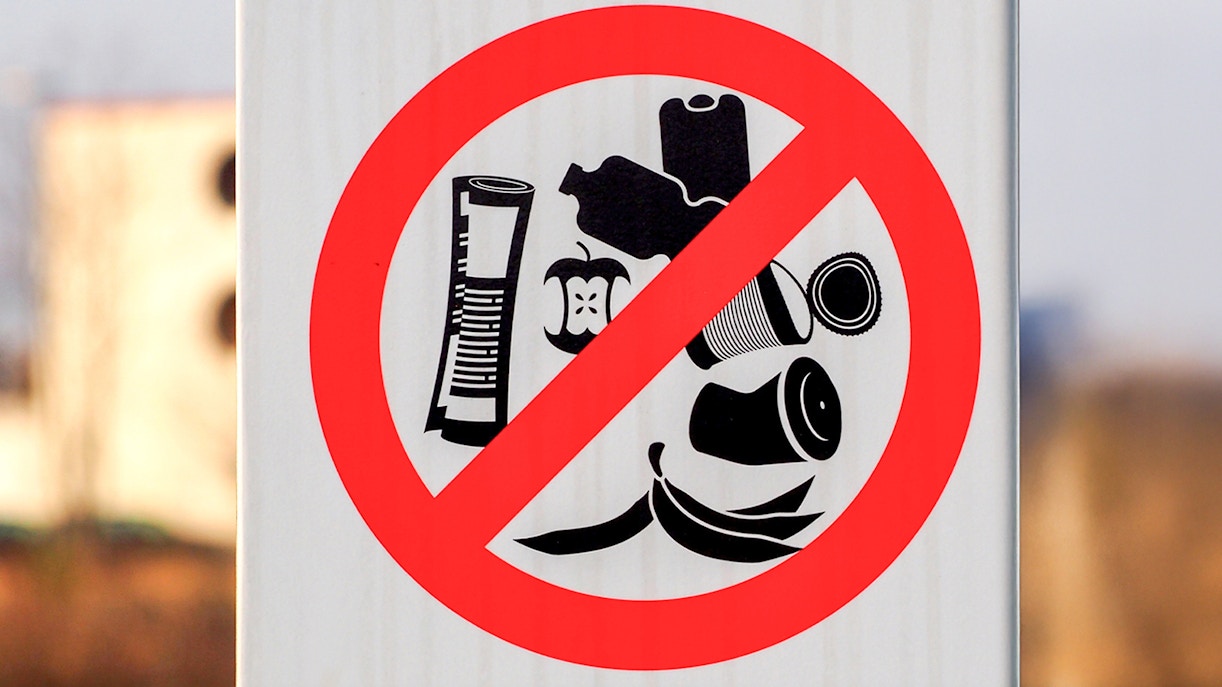 No littering sign in desert area with crossed-out trash symbols.