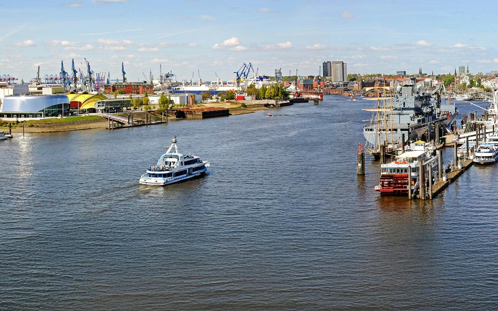 Hamburg Port with boats and skyline view, featuring cranes and waterfront buildings.