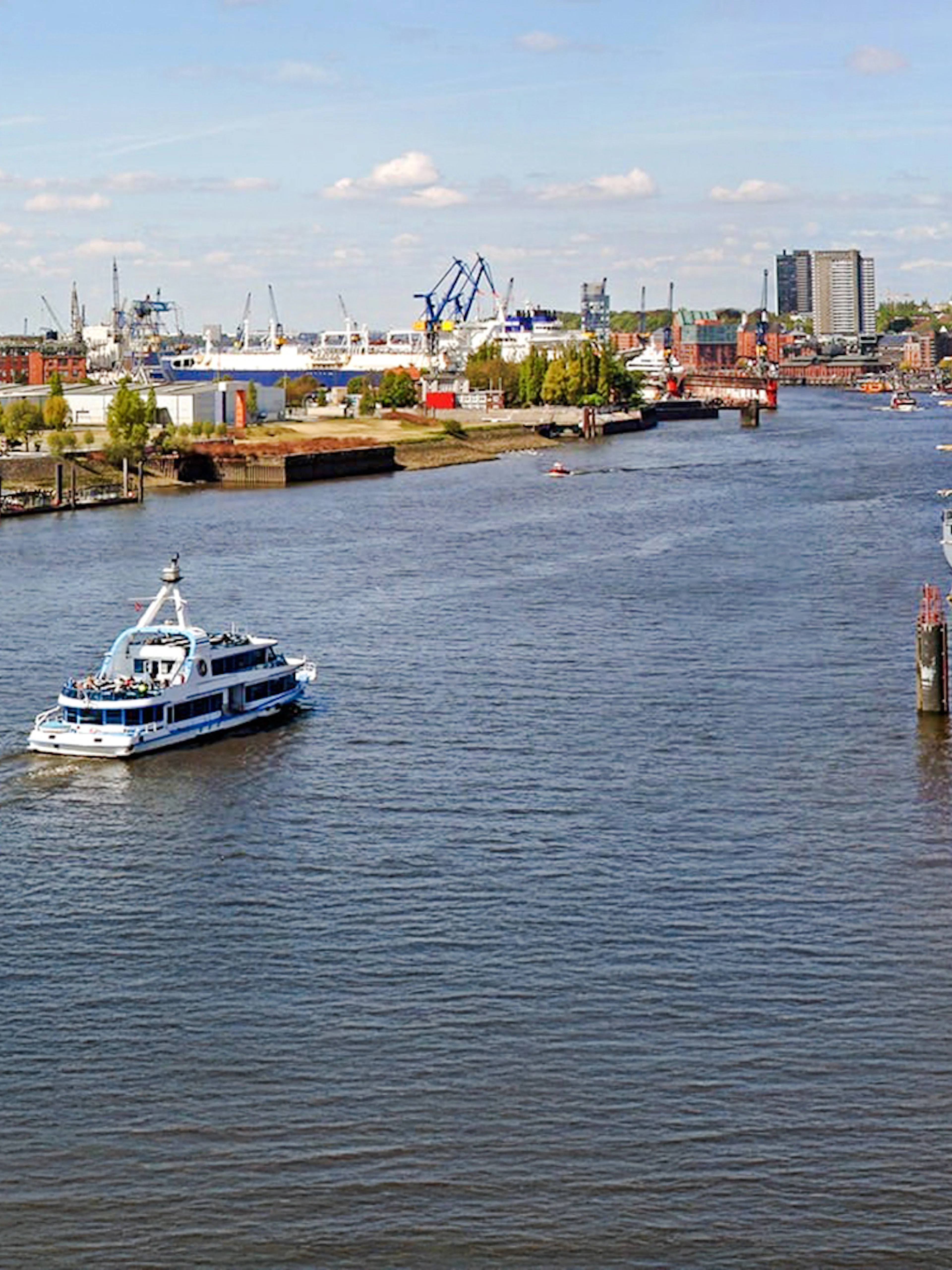Hamburg Port with boats and skyline view, featuring cranes and waterfront buildings.