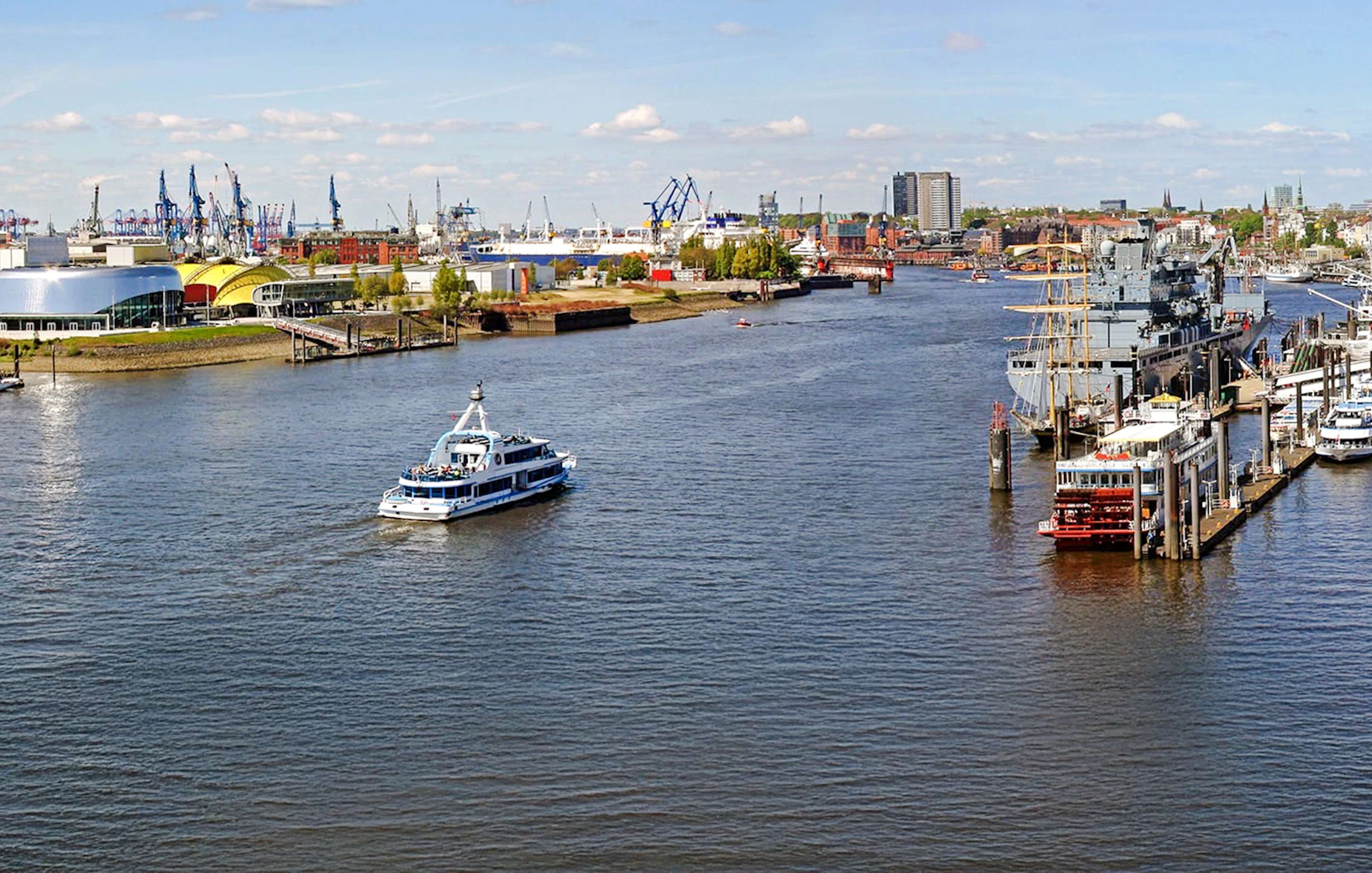 Hamburg Port with boats and skyline view, featuring cranes and waterfront buildings.