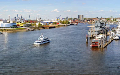 Hamburg Port with boats and skyline view, featuring cranes and waterfront buildings.