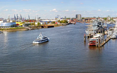 Hamburg Port with boats and skyline view, featuring cranes and waterfront buildings.