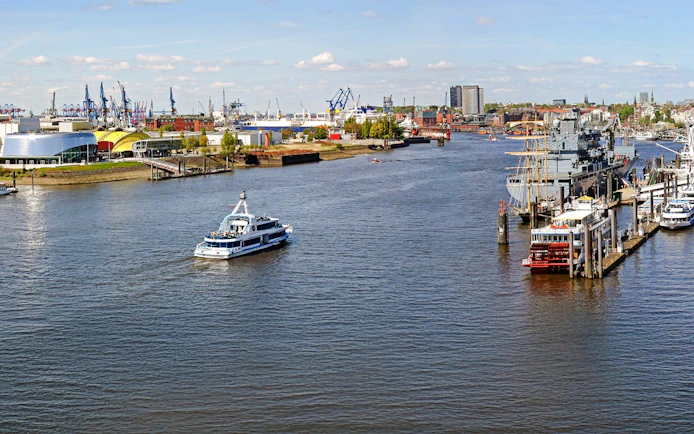 Hamburg Port with boats and skyline view, featuring cranes and waterfront buildings.