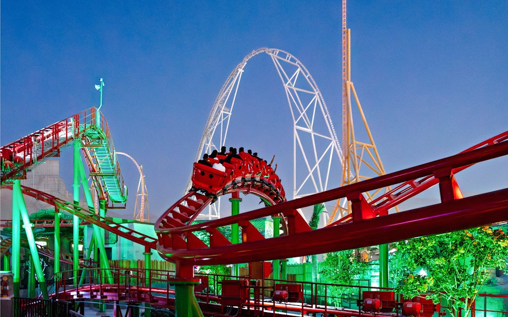 Roller coaster at Six Flags Qiddiya City with riders on a loop against a clear sky.
