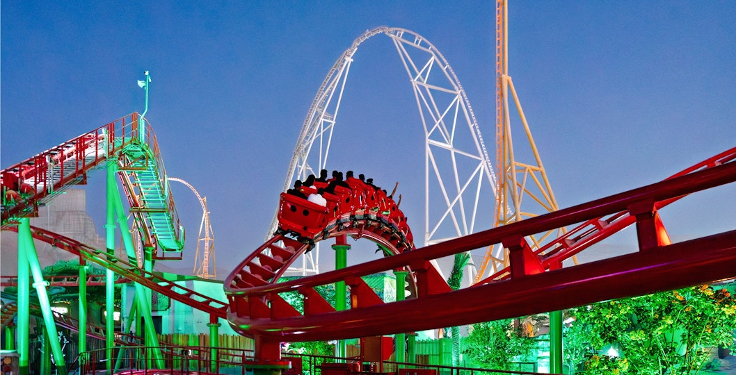 Roller coaster at Six Flags Qiddiya City with riders on a loop against a clear sky.