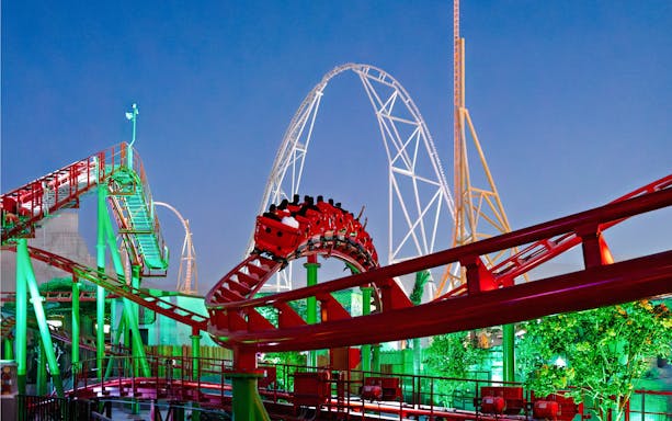 Roller coaster at Six Flags Qiddiya City with riders on a loop against a clear sky.