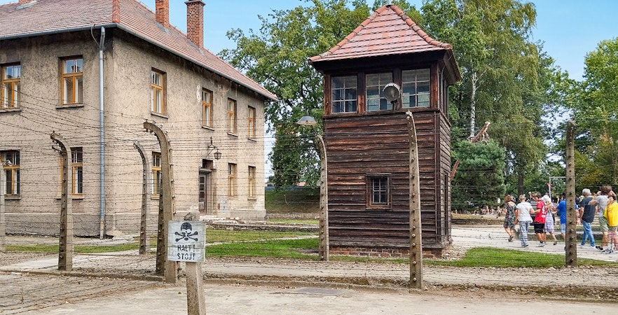 Watchtower and brick barracks at Auschwitz Birkenau I with visitors nearby.
