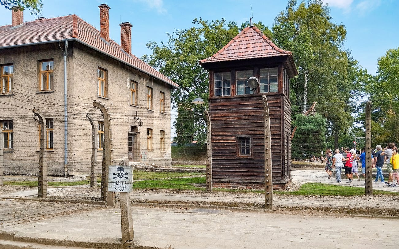 Watchtower and brick barracks at Auschwitz Birkenau I with visitors nearby.