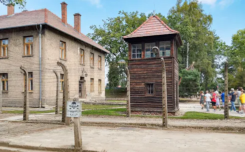 Watchtower and brick barracks at Auschwitz Birkenau I with visitors nearby.