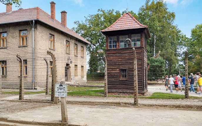 Watchtower and brick barracks at Auschwitz Birkenau I with visitors nearby.