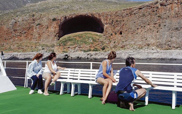 Guests on boat cruise viewing rocky landscape at Balos Lagoon, Greece.