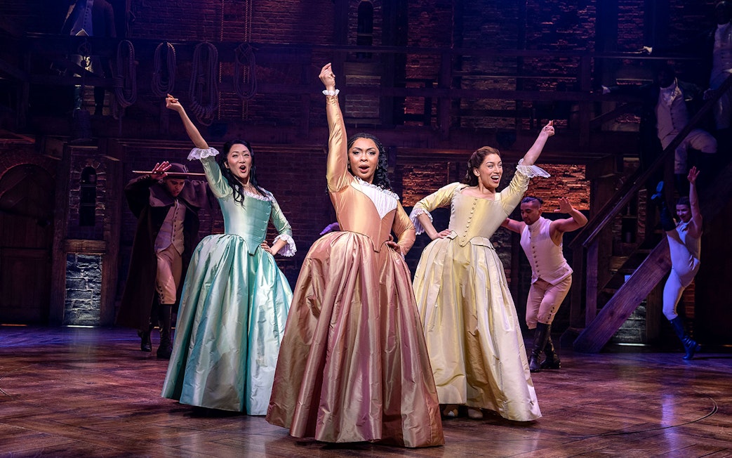 Performers in period costumes on stage during a Hamilton musical scene.