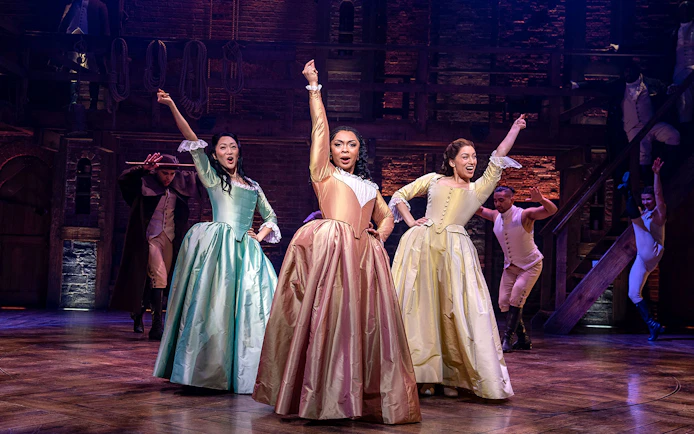 Performers in period costumes on stage during a Hamilton musical scene.
