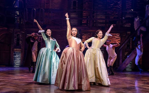 Performers in period costumes on stage during a Hamilton musical scene.