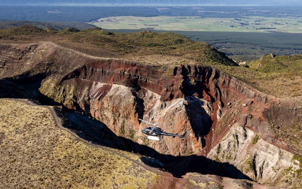 Helicopter flying over Mount Tarawera crater during guided summit walk in New Zealand.