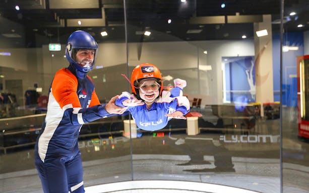 Child experiencing indoor skydiving with instructor at iFly Sydney.