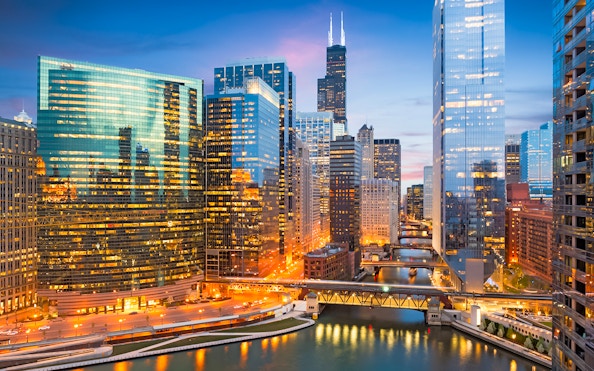 Chicago skyline with illuminated skyscrapers and river at dusk, Illinois, USA.