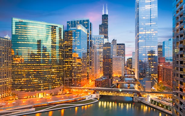 Chicago skyline with illuminated skyscrapers and river at dusk, Illinois, USA.