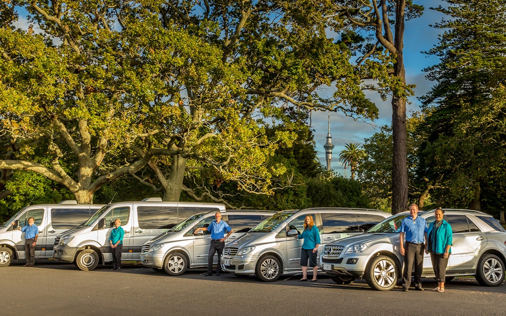 Tour vehicles and guides for Auckland to Hobbiton Movie Set Private Tour with Sky Tower in background.