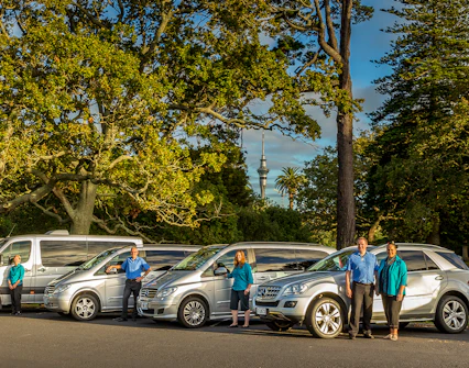 Tour vehicles and guides for Auckland to Hobbiton Movie Set Private Tour with Sky Tower in background.