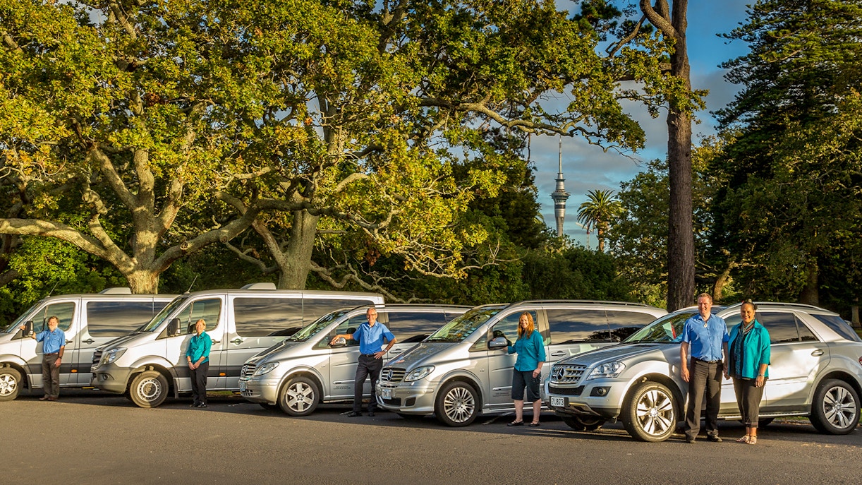Tour vehicles and guides for Auckland to Hobbiton Movie Set Private Tour with Sky Tower in background.