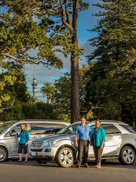 Tour vehicles and guides for Auckland to Hobbiton Movie Set Private Tour with Sky Tower in background.